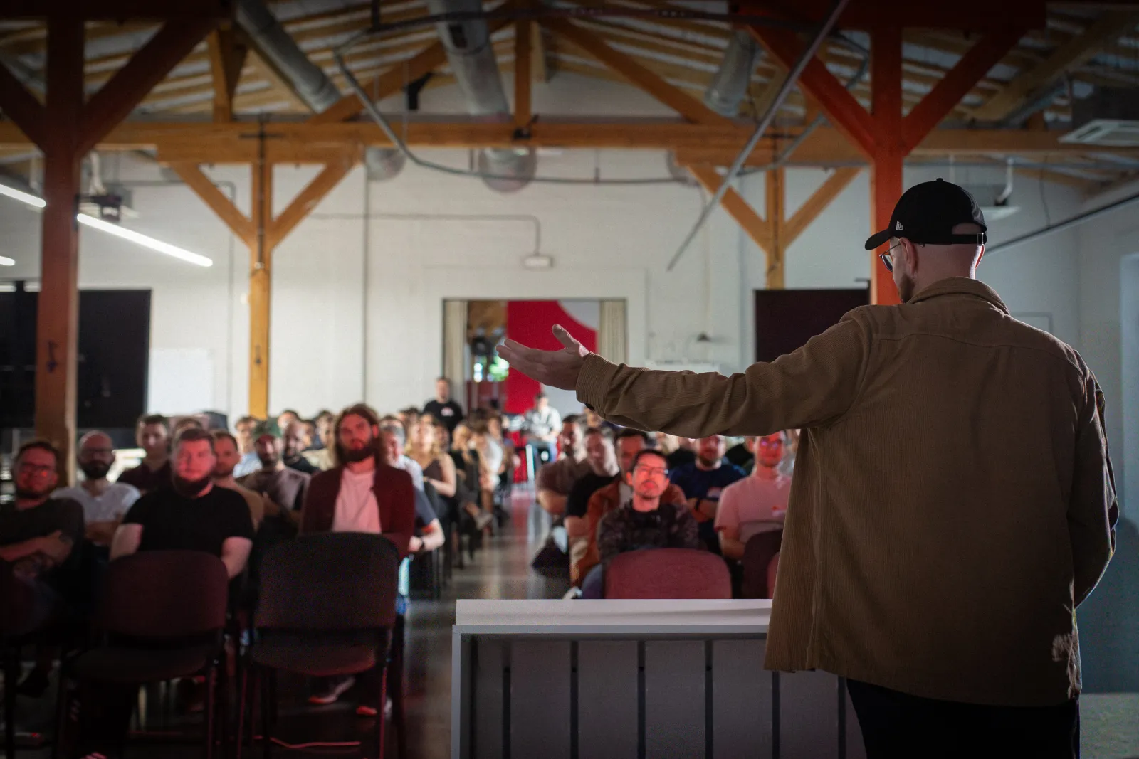 Szymon Chudy addressing a full room from the stage, arm outstretched mid-explanation